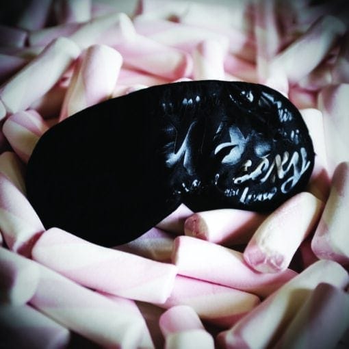 A black sleep mask with pink marshmallows on it.