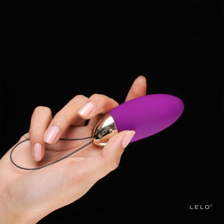 Hand holding a purple and gold pleasure vibrator with remote control, designed for intimate pleasure and sexual wellness, on a black background.