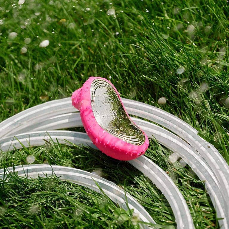 An eco-friendly compact mirror with a pink handle, placed on lush green grass with dew drops, ideal for personal grooming and beauty routines.