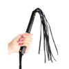 A hand holding a black leather whip with fringes.