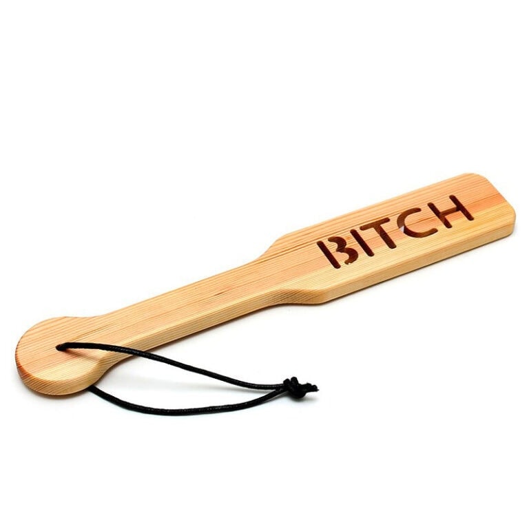 Wooden BDSM paddle with the word "Bitch" engraved, designed for adult spanking and BDSM activities, made of smooth wood with a comfortable handle and a black cord for hanging or storage.