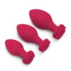 A set of three red sex toys on a white surface.