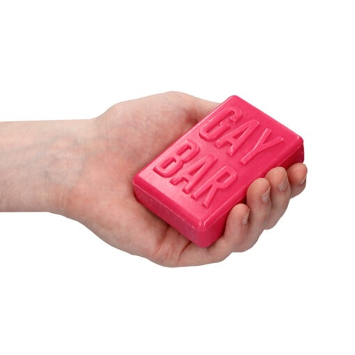 A hand holding a pink soap with the word gay bar on it.