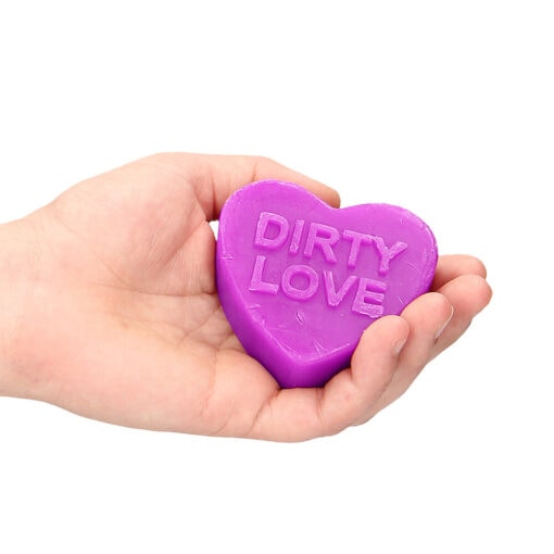 A hand holding a purple heart soap with dirty love written on it.