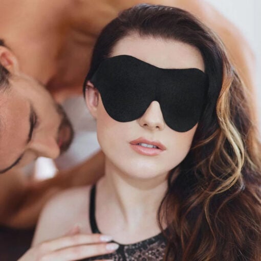 A woman is laying on a bed with a black eye mask.